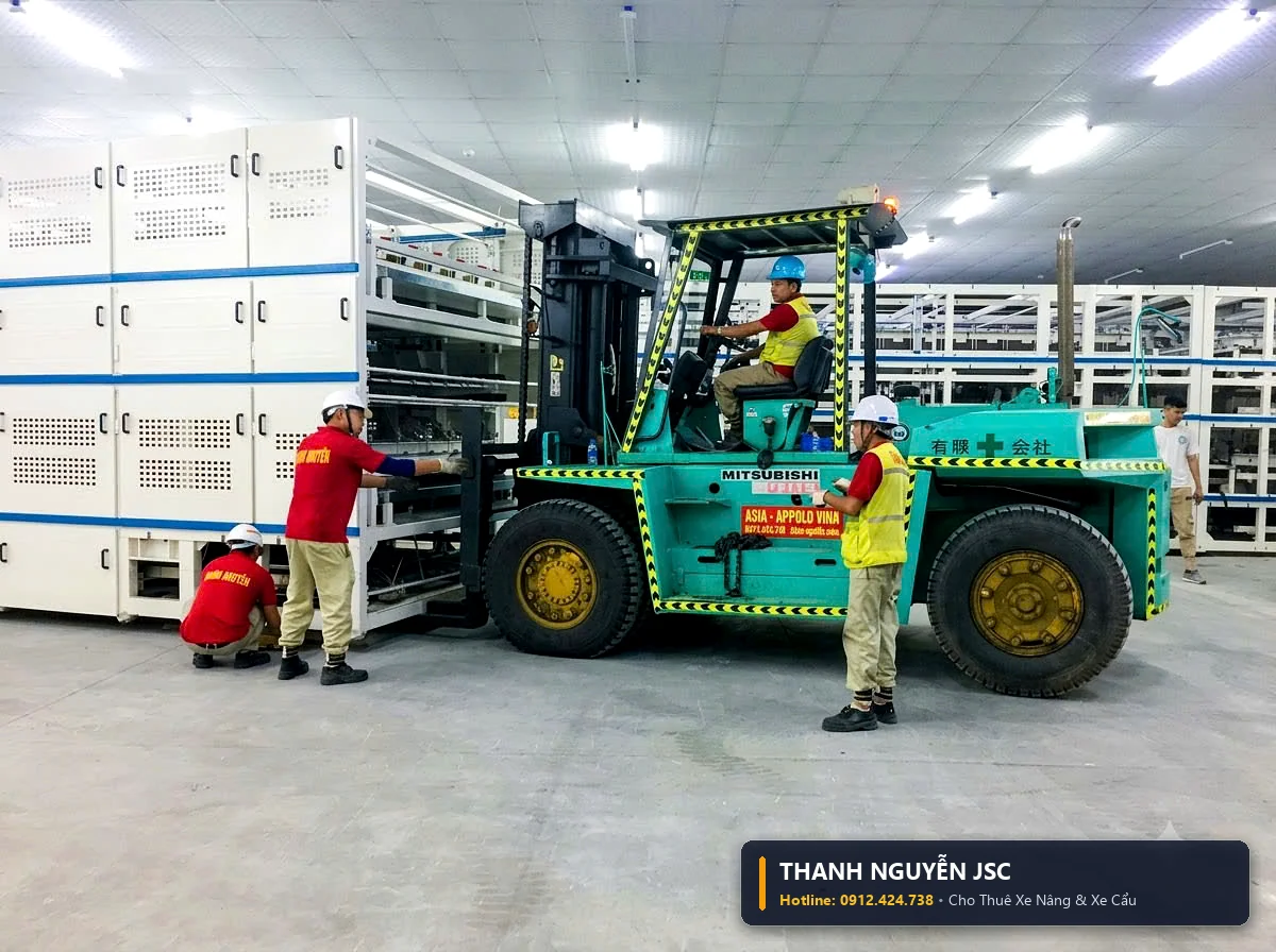Xe nâng hàng đưa khối máy móc công nghiệp áp sát dây chuyền tự động hóa với sự điều phối của công nhân THÀNH HUY HOÀNG tại Hải Dương