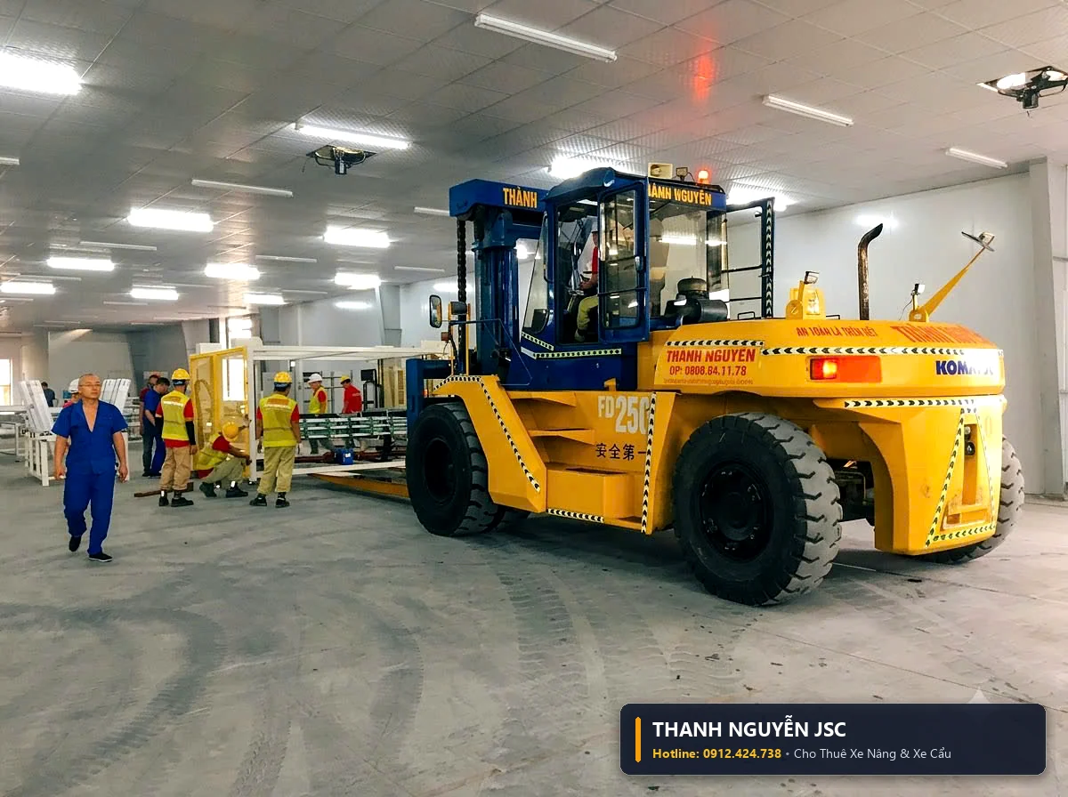 Xe nâng Komatsu 25 tấn vận chuyển khối máy lớn có công nhân chỉ đạo dẫn hướng